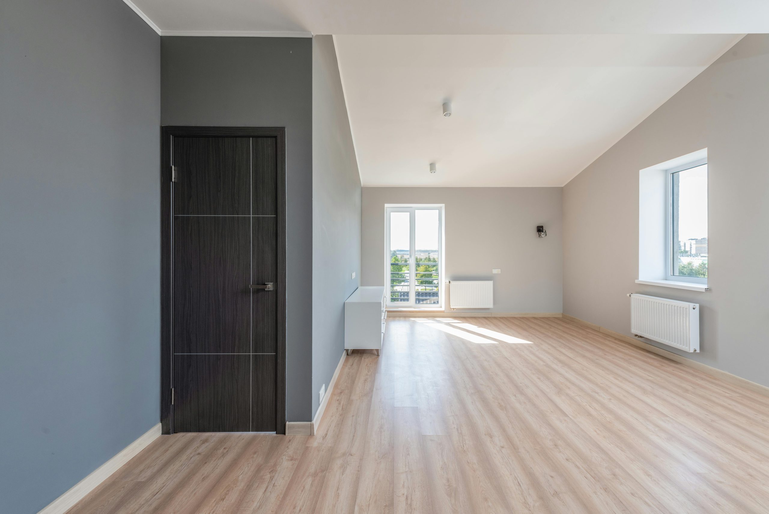 Spacious empty room with wooden flooring and large windows for ample natural light.